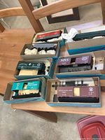 Overview of 7 model train cars in original blue and beige boxes with some packing material, including diverse box, reefer, and hopper types.