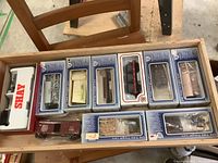 Photo of the lot showing a wooden drawer lined with 11 HO scale model train cars mostly in blue and white ITC Old Time Freight Cars boxes and one white/red Shay model in molded packaging, some cars unboxed.