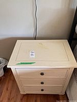 Front view of a yellow painted Ethan Allen nightstand with three drawers and round black metal knobs on hardwood flooring.