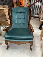Front view of the wing back chair showing tufted green upholstery, wooden frame with cane sides, and seat cushion.