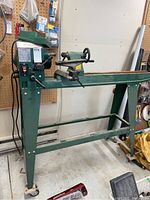 Overview of wood lathe on green stand with swivel casters