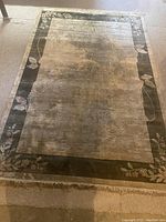 Full view of taupe and black silk oriental rug showing overall design and condition, including frayed fringe.
