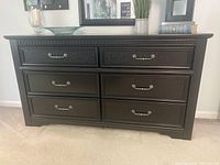 Front view of black dresser showing six drawers with brushed nickel hardware and etched detailing on top drawers.