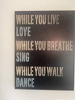 Canvas with inspirational quote emphasizing living, loving, breathing, singing, walking, and dancing in distressed white and light blue lettering on black background.