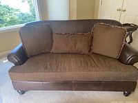 Front view of brown leather and fabric loveseat with three pillows