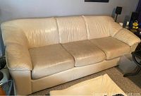 Off white contemporary leather sofa with visible wear areas on cushions, no tears, shown from front angle.
