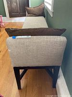 Photo showing the rear view of the upholstered bench with two brown cushions, beige seat upholstery, and dark wooden legs and frame.