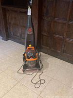 Front view of full unit with hose and power cord coiled, showing upright deep cleaner on floor.