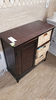 Front angle view of wood cabinet showing dark brown finish, single door on left, two wicker drawers on right.