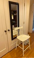 White wooden chair positioned in front of a closed closet door with over-the-door mirror behind it