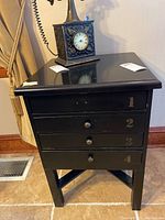 Front view of the black wooden side table with four drawers numbered 1 through 4 in beige stenciling.
