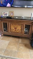 Full front view of wood credenza with marble top and decorative floral pattern on center door, wire mesh on side doors.