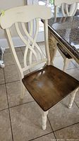 Front and side view of a wooden dining chair with white painted frame and brown seat showing minor scratches and wear on the seat surface.