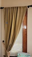 Single rod pocket beige drape panel hung on window with rope tieback