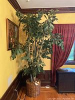 Full view of the 8-foot tall faux tree with green leaves in woven wicker basket planter against yellow wall and red curtains.