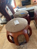 Two round foot stools with carved wooden lattice bases and padded fabric tops with floral pattern, placed on floor