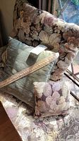 Three decorative throw pillows arranged on a floral pattern chair near window showing fabric texture and colors