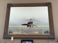 Large rectangular wall mirror with an ornate brown wooden frame hanging on a wall, showing a visible crack in the mirror glass.