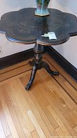 Full view of wood side table with scalloped top and painted floral design on top surface.