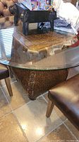 Glass top with carved pedestal base and part of chairs visible