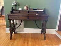 Front view of wood writing desk showing two large front drawers and four small top drawers. Curved metal braces are visible connecting the legs for support.