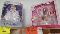 Wider shot of the two Barbie doll sets in packaging on a shelf, showing both the Cinderella and Wedding Cake Barbie sets.