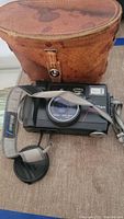 Nikon Action Touch camera with neck strap and lens cap, placed in front of brown leather case.