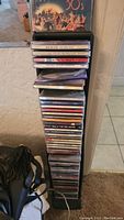 Stack of assorted CDs placed vertically in a slim CD rack against a wall, showing many titles and cases