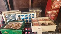 Photo showing multiple boxes of Christmas ornaments in different colors: blue, gold, red, with packaging visible.