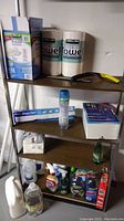 Shelf with Kirkland paper towels, flushable wipes box, spray bottles, gloves, and plastic utensils visible