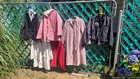 Full view of approximately 6 jackets hanging on a clothesline, various colors including dark gray, pink, beige, white, and red.