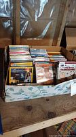 Photo of a box containing assorted DVDs including visible titles: Charlie Brown Thanksgiving, Winnie the Pooh, Bernstein Bears, National Geographic.
