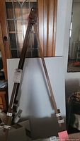Wooden folding easel with adjustable height leaning against a wooden door and cabinet.