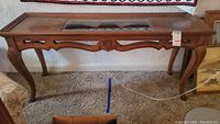 Front view of wood entry table showing carved legs and apron, with glass insert top.