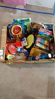 Photo showing box with various toys including bubble wands, small balls, xylophone, sidewalk chalk and other toys packed together.