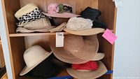 Multiple women's hats in wooden shelving unit including cream hat with polka dot ribbon, tan large brim sunhat, black hats and decorative floral hats.