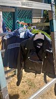 Photo showing two kids jackets hanging outside: a black leather All American Rider jacket with zipper and belt detail, the leather jacket has a stain, and a blue NFL Seahawks jacket beside it.
