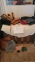 Multiple handbags and purses arranged on a table and floor, showing different sizes, styles, and colors