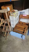 Photo of wooden shelves, plastic storage drawers, wooden boxes and miscellaneous storage items grouped on concrete floor.