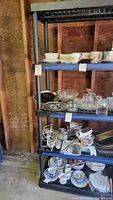 Two black plastic shelving units with various kitchenware items arranged on the shelves, showing size and structure. Shelves are stackable and have five levels each.