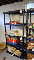 Two tall black plastic shelving units with multiple slatted shelves. Shelves are filled with various household items for display only, items not included in sale.