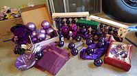 Lot overview showing purple hanging ornaments packed and loose, purple beads, purple striped cloth, purple stuffed animal, and decorative pieces on floor.