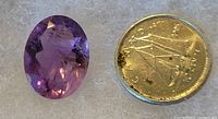 Photo shows a large faceted oval amethyst gemstone positioned next to a Canadian one-dollar coin to show size.
