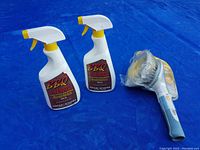 Two BBQ Cleaner bottles and one patio furniture cleaning brush on blue background.