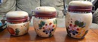 Set of three floral ceramic canisters with clamp lids on wooden surface in front of a sofa.