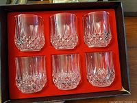 Six clear crystal glasses with decorative cut patterns seated in red cushioned box interior.