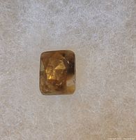 Photo of a rectangular cut golden sheen sapphire gemstone on a soft textured light background.