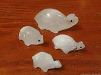 Photo showing four white stone hand carved turtle figurines with black eyes, varying slightly in size and shape, arranged on a wooden surface.