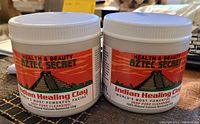 Photo of two unopened containers of Aztec Secret Indian Healing Clay with colorful labels showing product name and details.