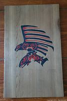 Full view of the wooden panel featuring Indigenous art of an eagle and fish in red and black on natural wood.
